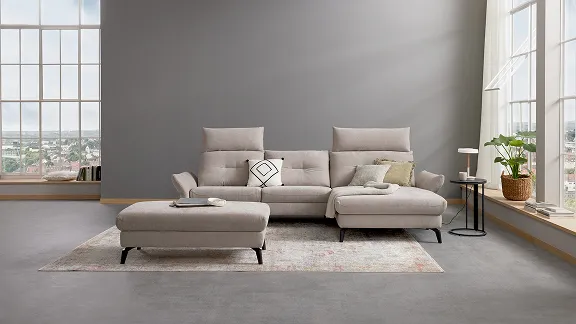 Beiges Sofa-Set in modernem Wohnzimmer mit großen Fenstern und hellem Teppich, umgeben von Pflanzen und stilvollen Kissen.